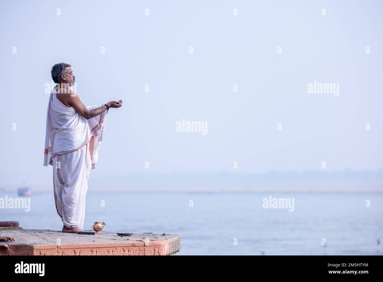 Varanasi, India: Portrait of Unidentified Indian sadhu baba worshiping lord sun in traditional white dress on ghat near river ganges in varanasi city. Stock Photo