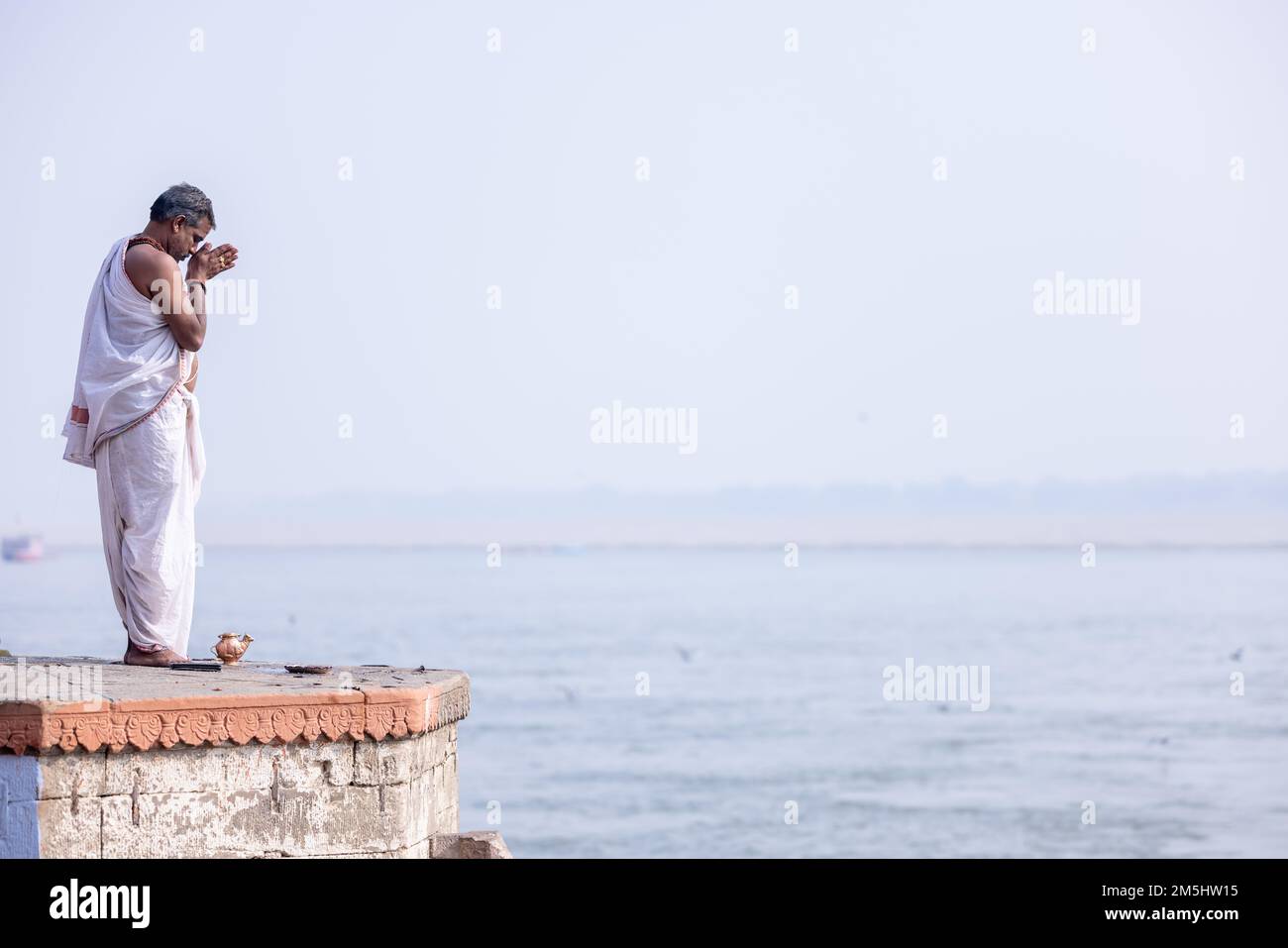 Varanasi, India: Portrait of Unidentified Indian sadhu baba worshiping lord sun in traditional white dress on ghat near river ganges in varanasi city. Stock Photo