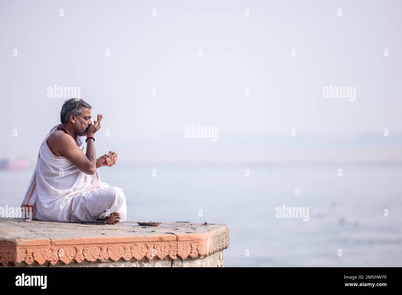 Varanasi, India: Portrait of Unidentified Indian sadhu baba worshiping lord sun in traditional white dress on ghat near river ganges in varanasi city. Stock Photo