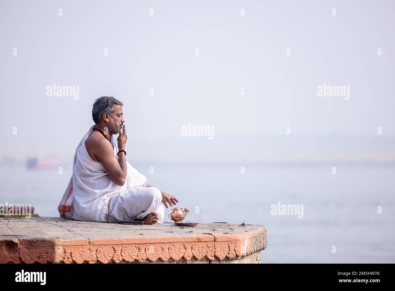 Varanasi, India: Portrait of Unidentified Indian sadhu baba worshiping lord sun in traditional white dress on ghat near river ganges in varanasi city. Stock Photo