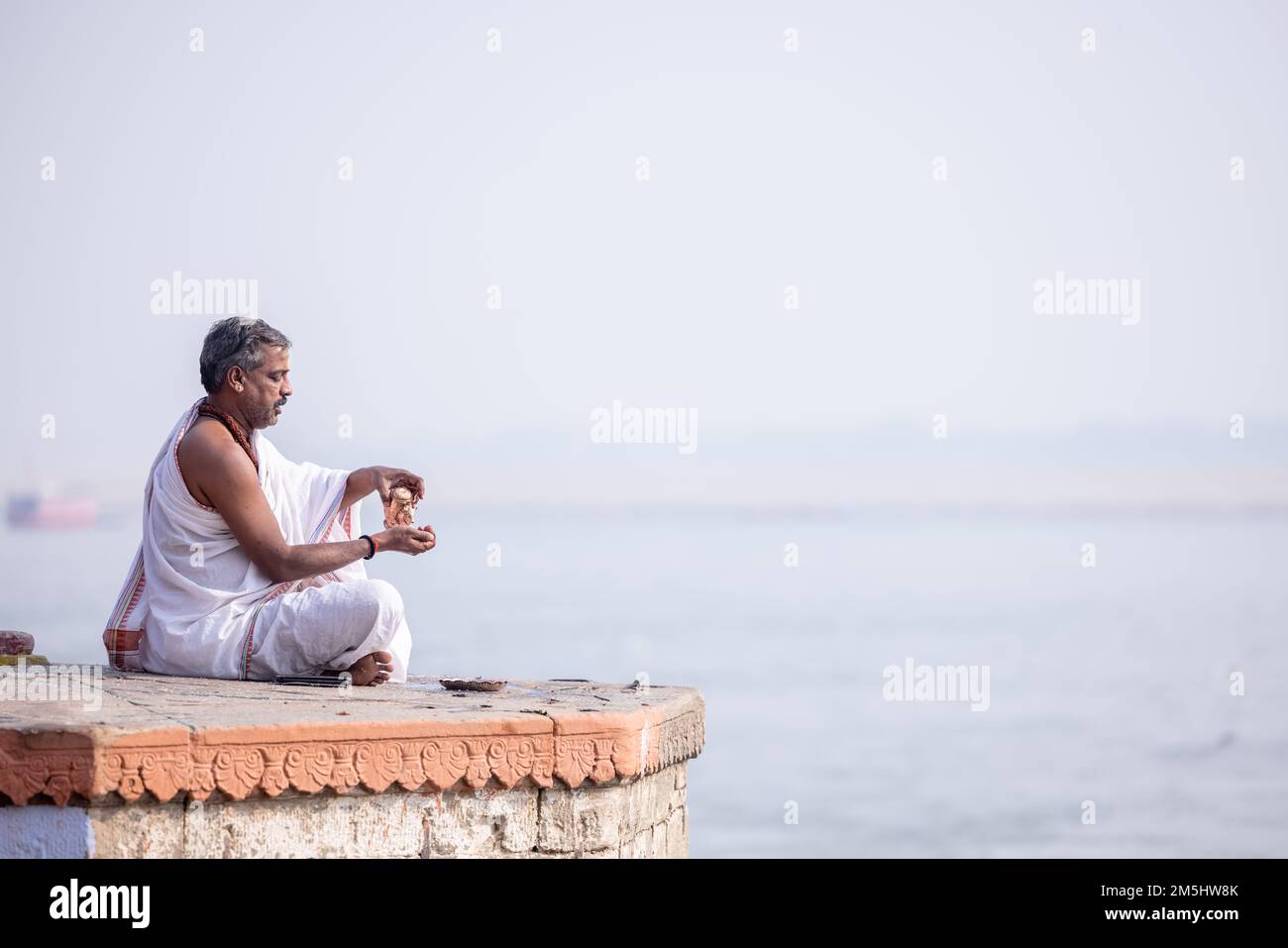 Varanasi, India: Portrait of Unidentified Indian sadhu baba worshiping lord sun in traditional white dress on ghat near river ganges in varanasi city. Stock Photo