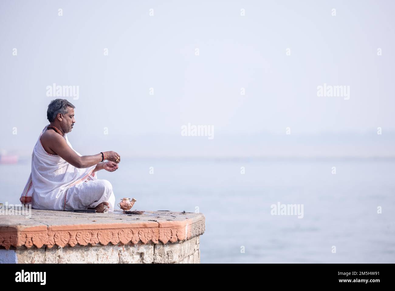 Varanasi, India: Portrait of Unidentified Indian sadhu baba worshiping lord sun in traditional white dress on ghat near river ganges in varanasi city. Stock Photo