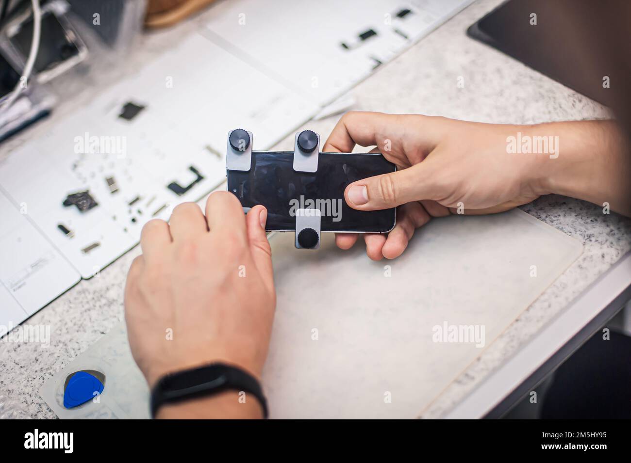 In the electronics repair shop, the master repairs, cleans, controls, arranges the smartphone. Uses equipment and tools for work. Workplace top view, Stock Photo