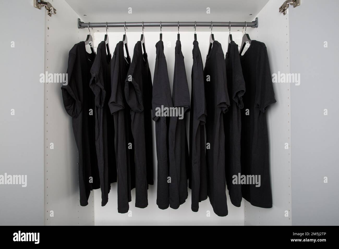 black tshirts hang on a clothes rail in a white wardrobe. all tshirts