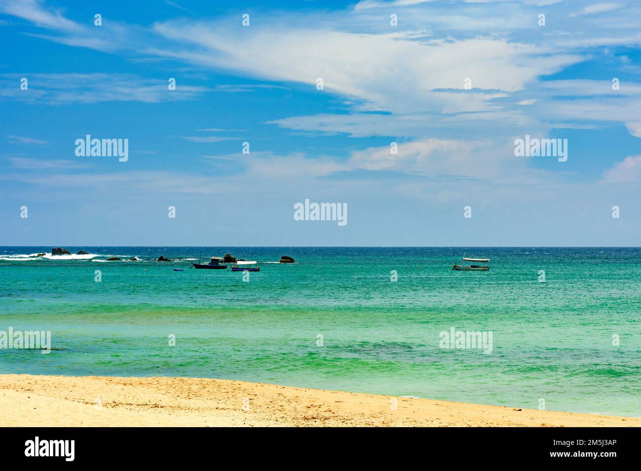 Wooden fishing boats on the colorful waters of Itapua beach in Salvador, Bahia with rocks and waves in the background Stock Photo
