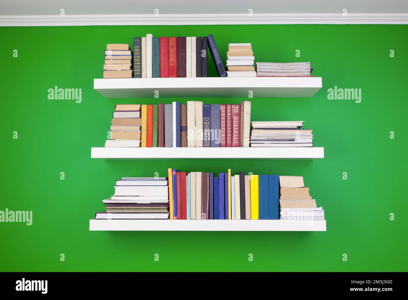 neat stacks and rows of books on white shelves against a green wall Stock Photo