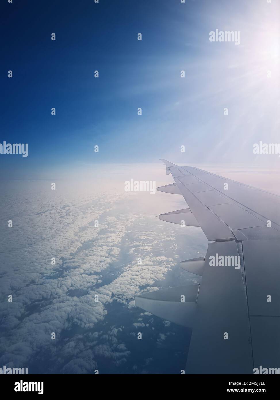 Plane flight above the clouds. Blue skyline and airplane wing seen through the window Stock Photo