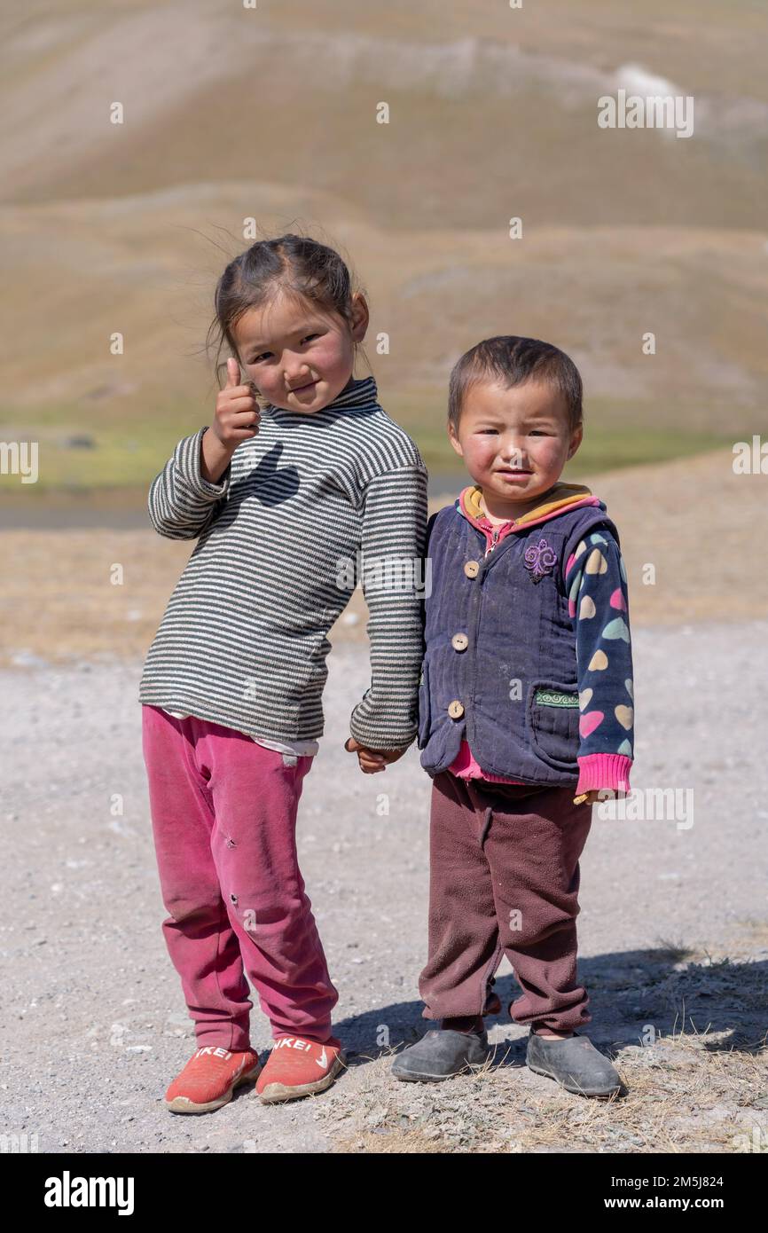 Achik Tash, Kyrgyzstan - 08 29 2019 : Kyrgyz brother and sister young children holding hands, smiling and giving thumb up at Lenin Peak base camp Stock Photo