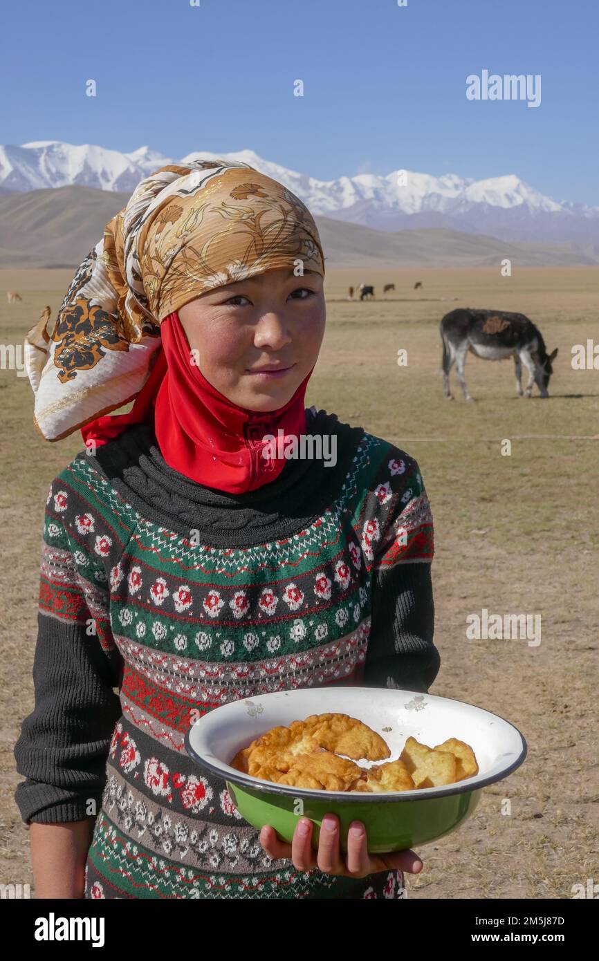 Achik Tash, Kyrgyzstan - 08 30 2018 : Portrait of young Kyrgyz girl showing traditional hospitality by offering doughnuts in the rural countryside Stock Photo
