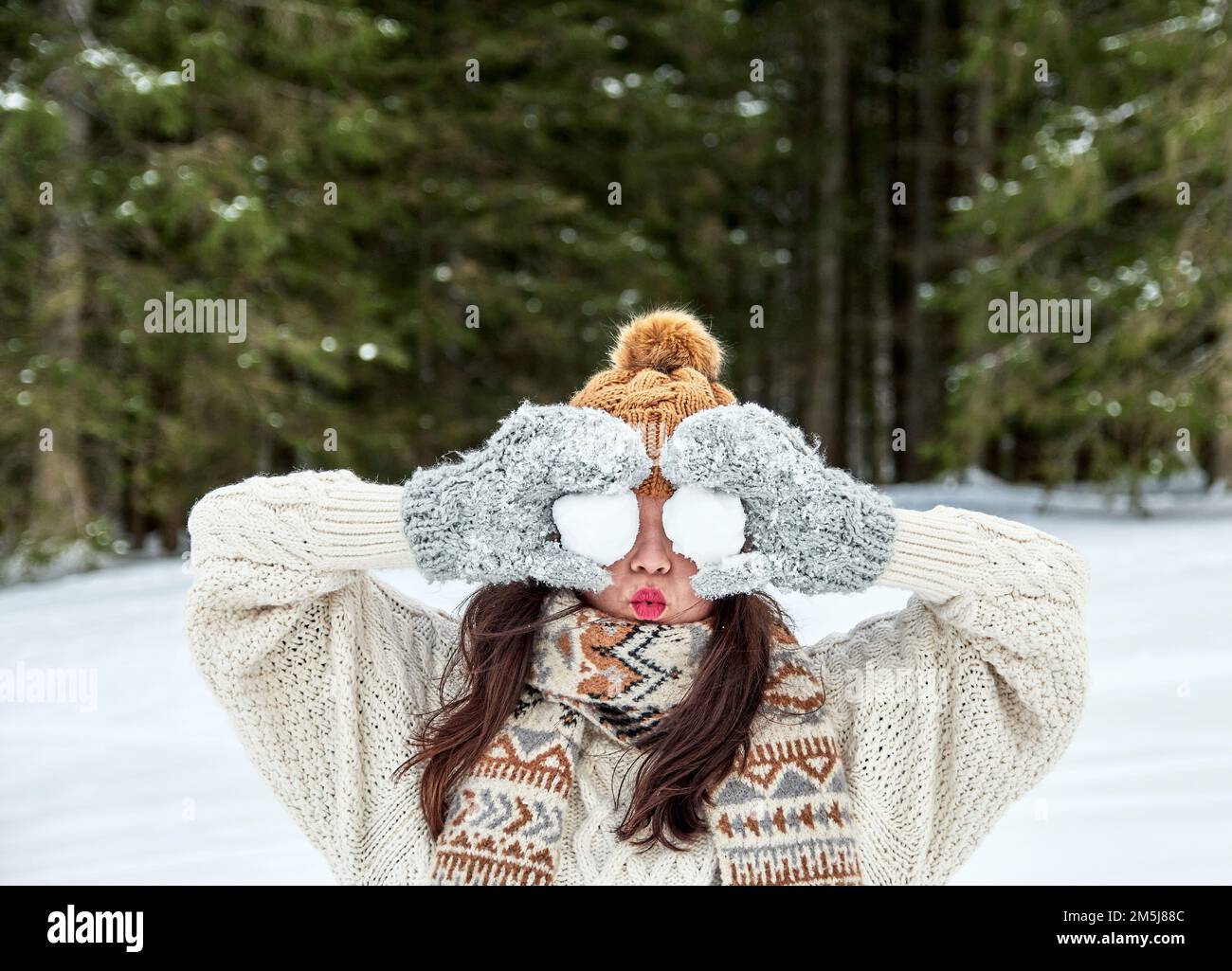 A girl in a warm winter hat and gloves holding two snowballs in front