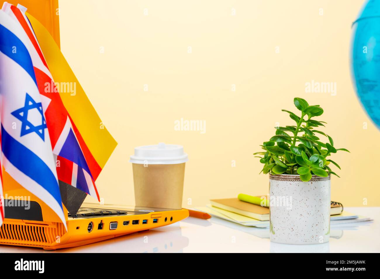 International online education. Laptop, notebooks, a globe, a cup of coffee and flags of different country on a beige background with copy space. Conc Stock Photo