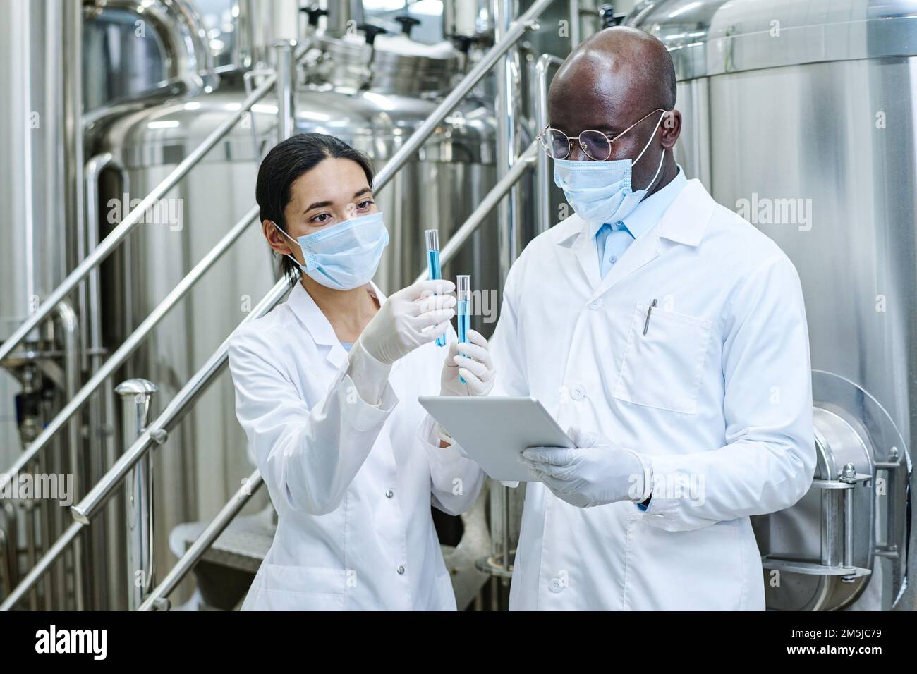 Couple of scientists in white coats examining liquid in test tubes and ...