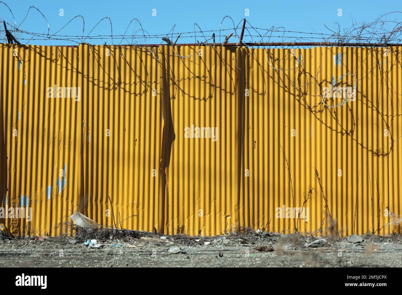 Yellow corrugated metal texture wall with barbed wire in industrial area of the Bronx Stock Photo
