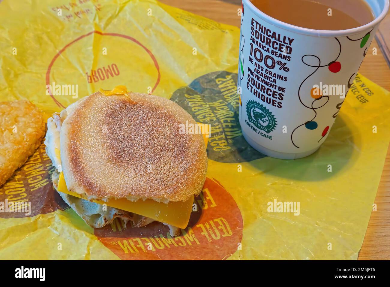 Paper cup of Ethically sourced coffee and Egg McMuffin on a yellow wrapper. Stock Photo