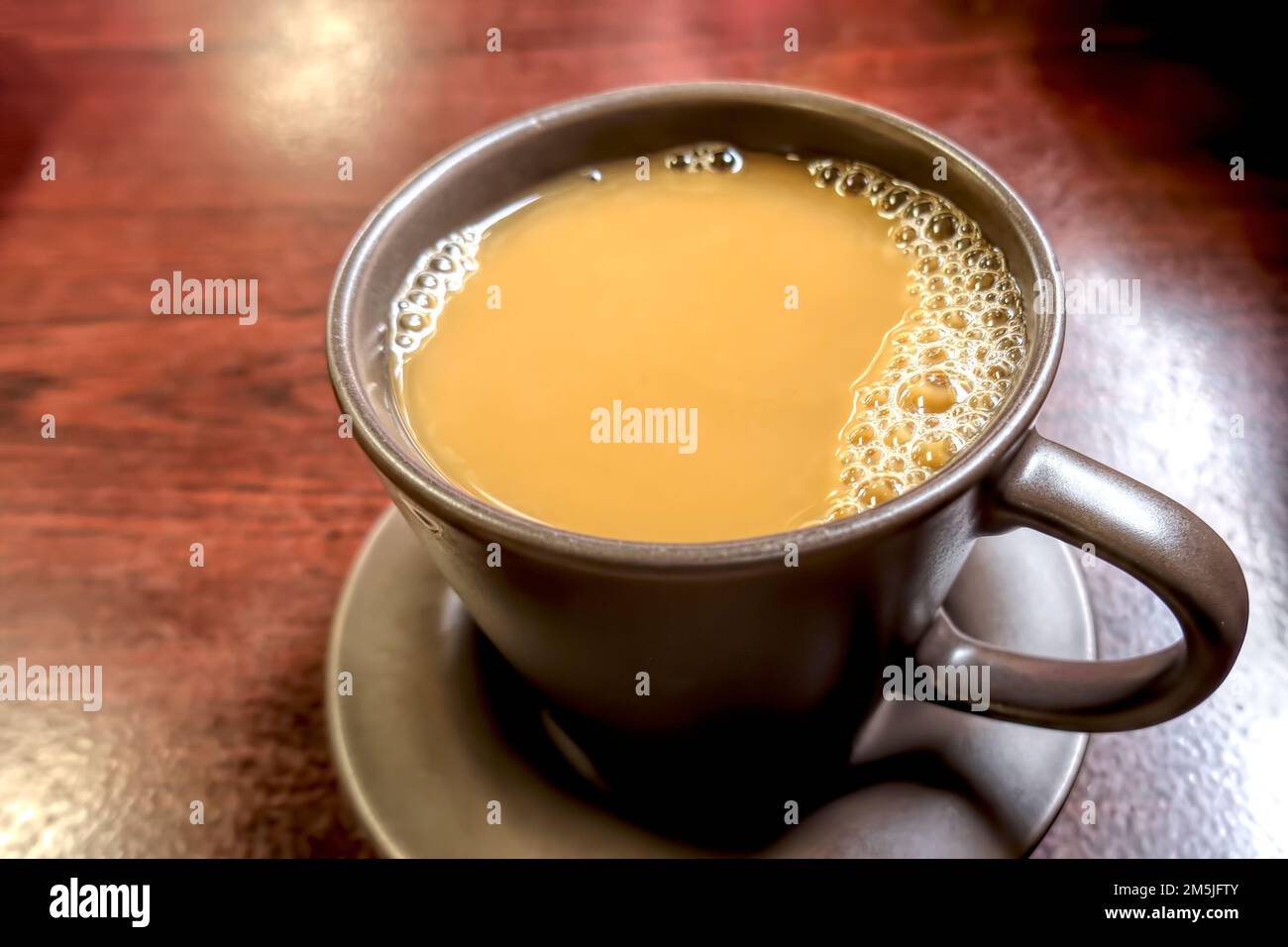 Cup of coffee with cream in a brown stoneware mug - closeup with bubbles. Stock Photo