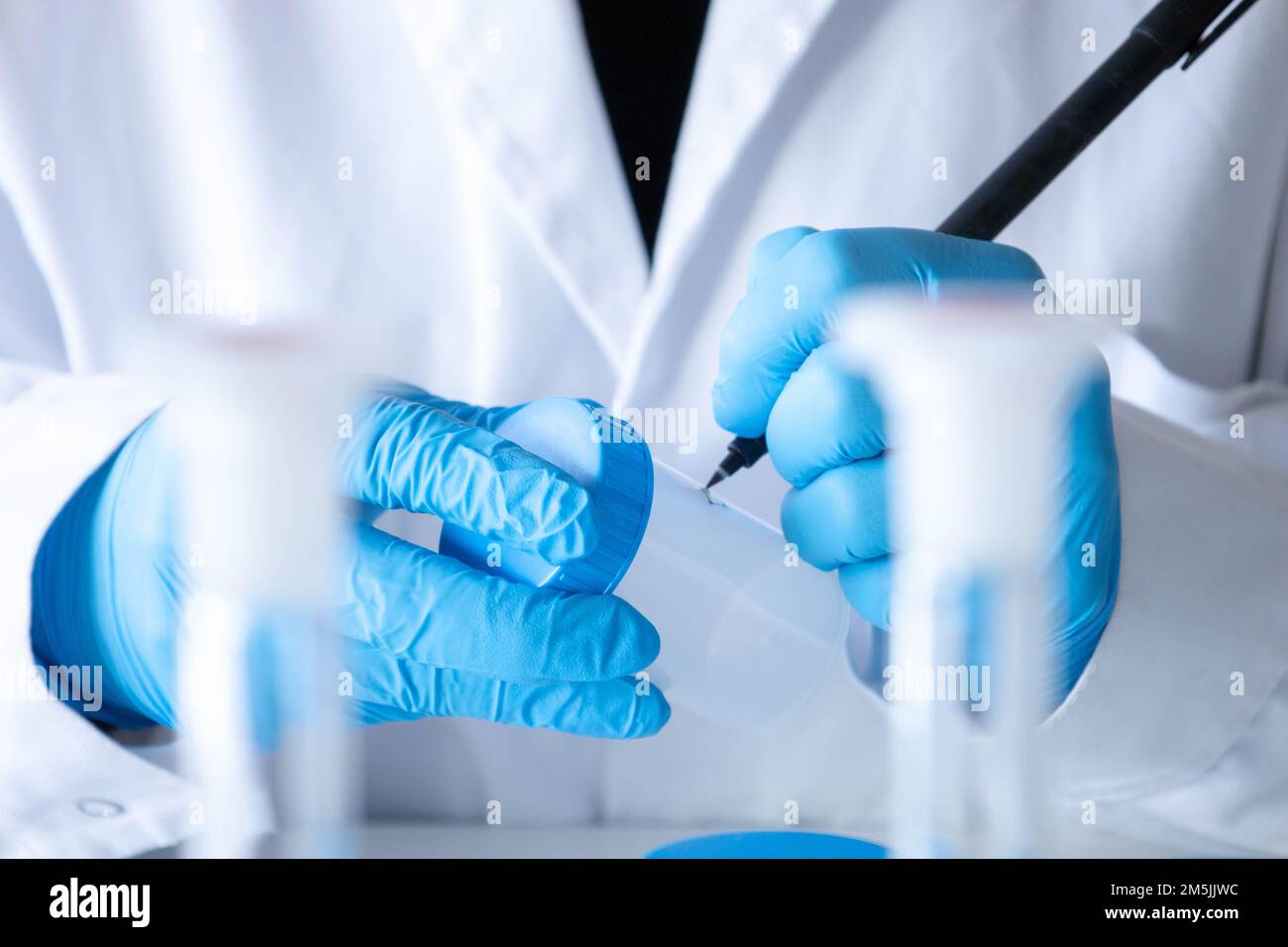 Left handed female scientist labeling samples with blue gloves and equipment. Lab technician writing. Development and medical research. Stock Photo