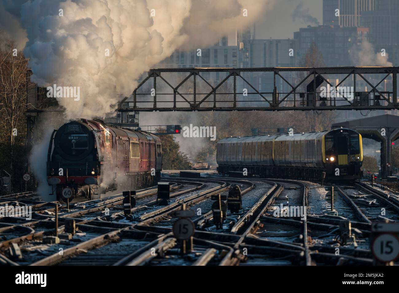 Old and new, an electric locomotive, beside steam train 46233 approaching Clapham Junction on a cold December morning, London skyline in background Stock Photo