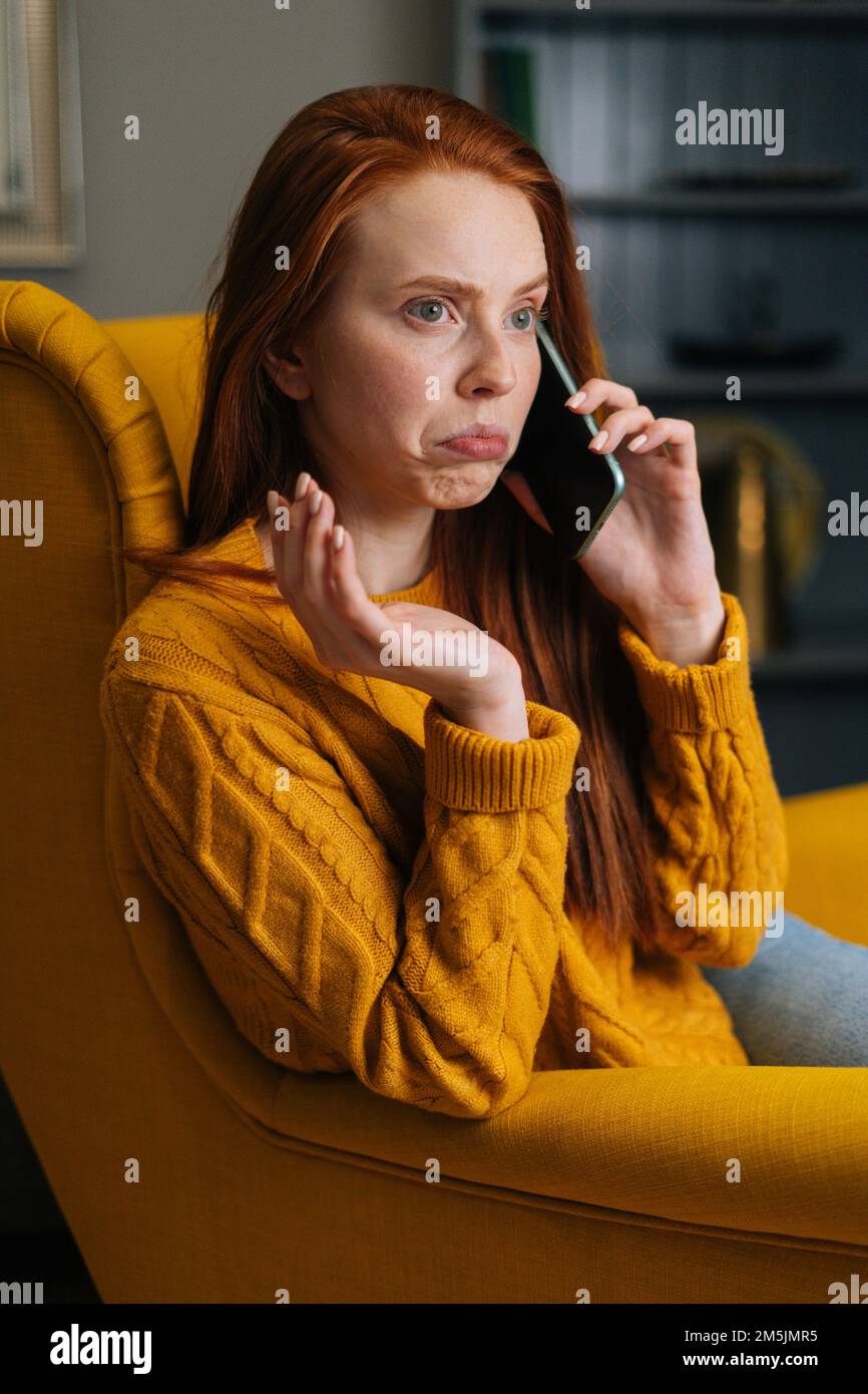 Vertical portrait of baffled young woman talking on smartphone sitting