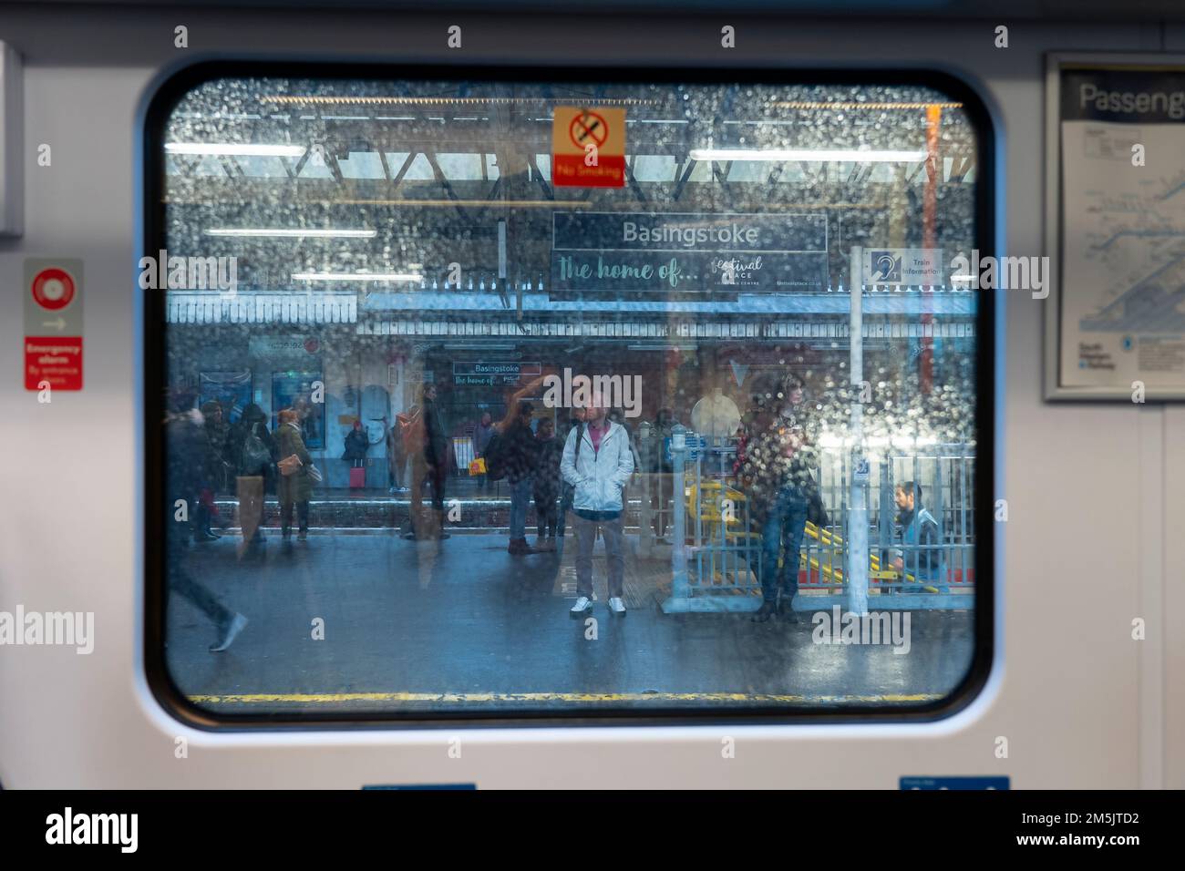 Looking out of raindrop covered train carriage window at people standing on a railway station platform. Concept: delayed services, train delays. UK Stock Photo