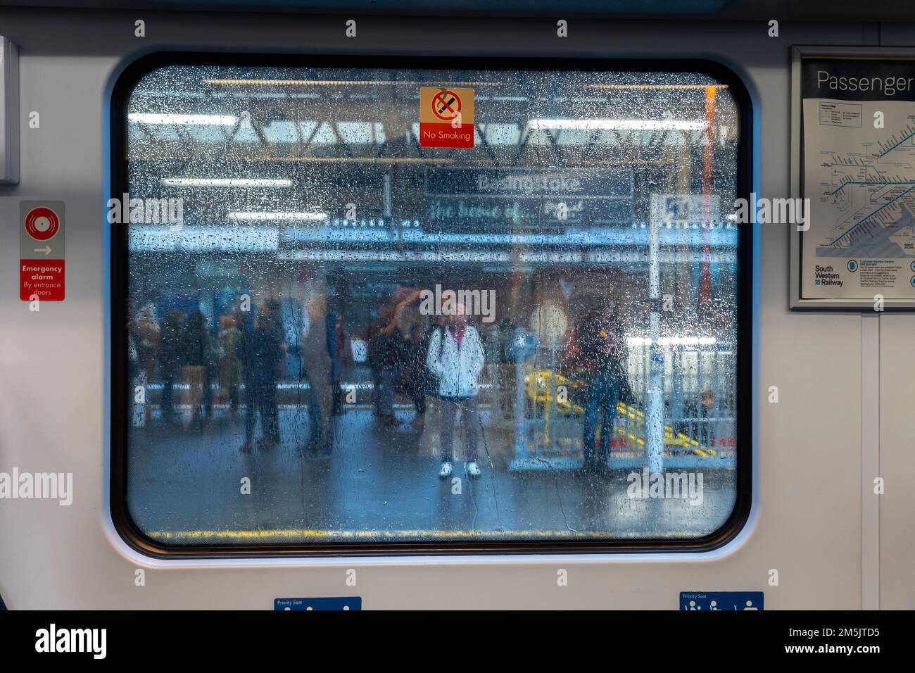 Looking out of raindrop covered train carriage window at out of focus people standing on a railway station platform. Concept: delayed services. UK Stock Photo