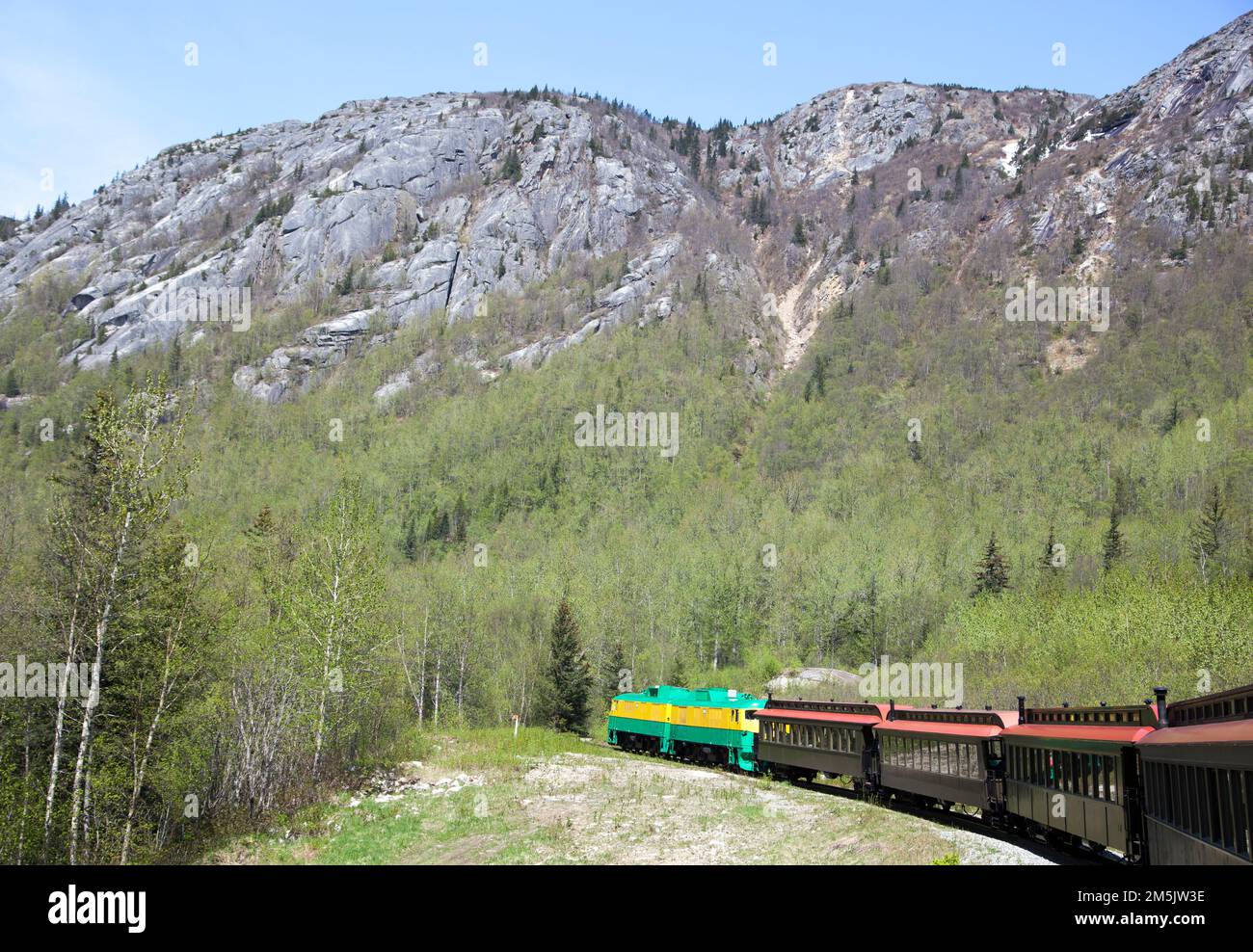 The springtime view of a train going through White Pass, the mountain pass through Boundary Ranges mountains reaching 873 meters elevation (Alaska). Stock Photo