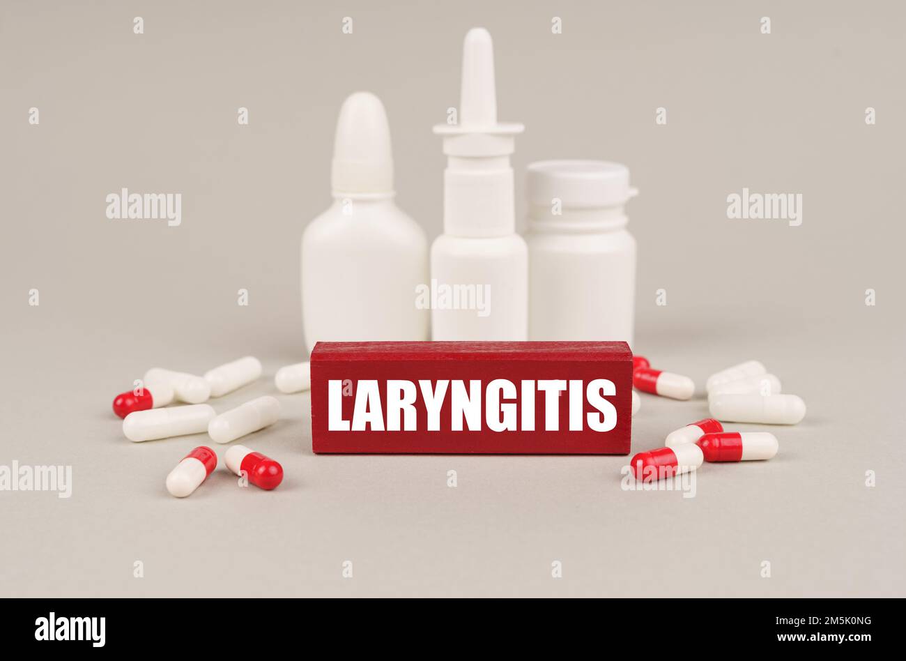 Medical concept. On a gray surface are pills, white jars and a red wooden block with the inscription - Laryngitis Stock Photo