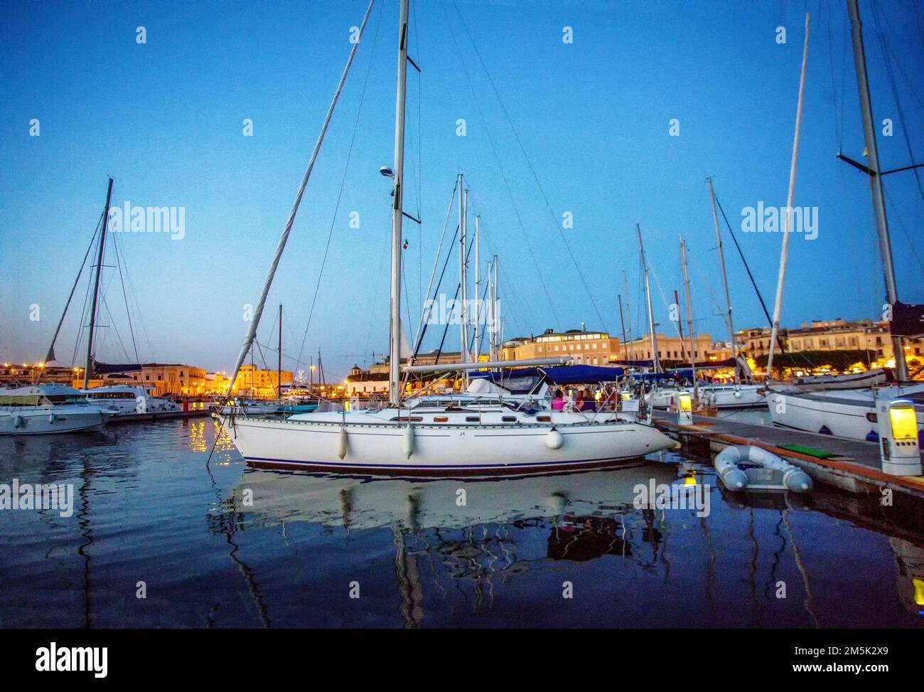 Sailboats in harbor of Siracuse (behind Old town as island).   On second boat - Italian people  in distance (unrecognizable persons)  celebrate weeken Stock Photo