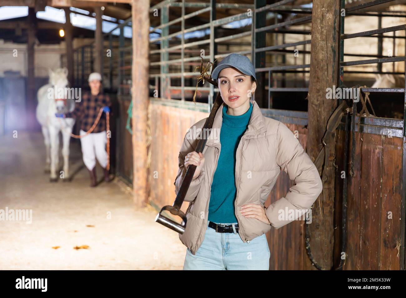 Young female stable worker carrying pitchfork to stack hay for horses ...