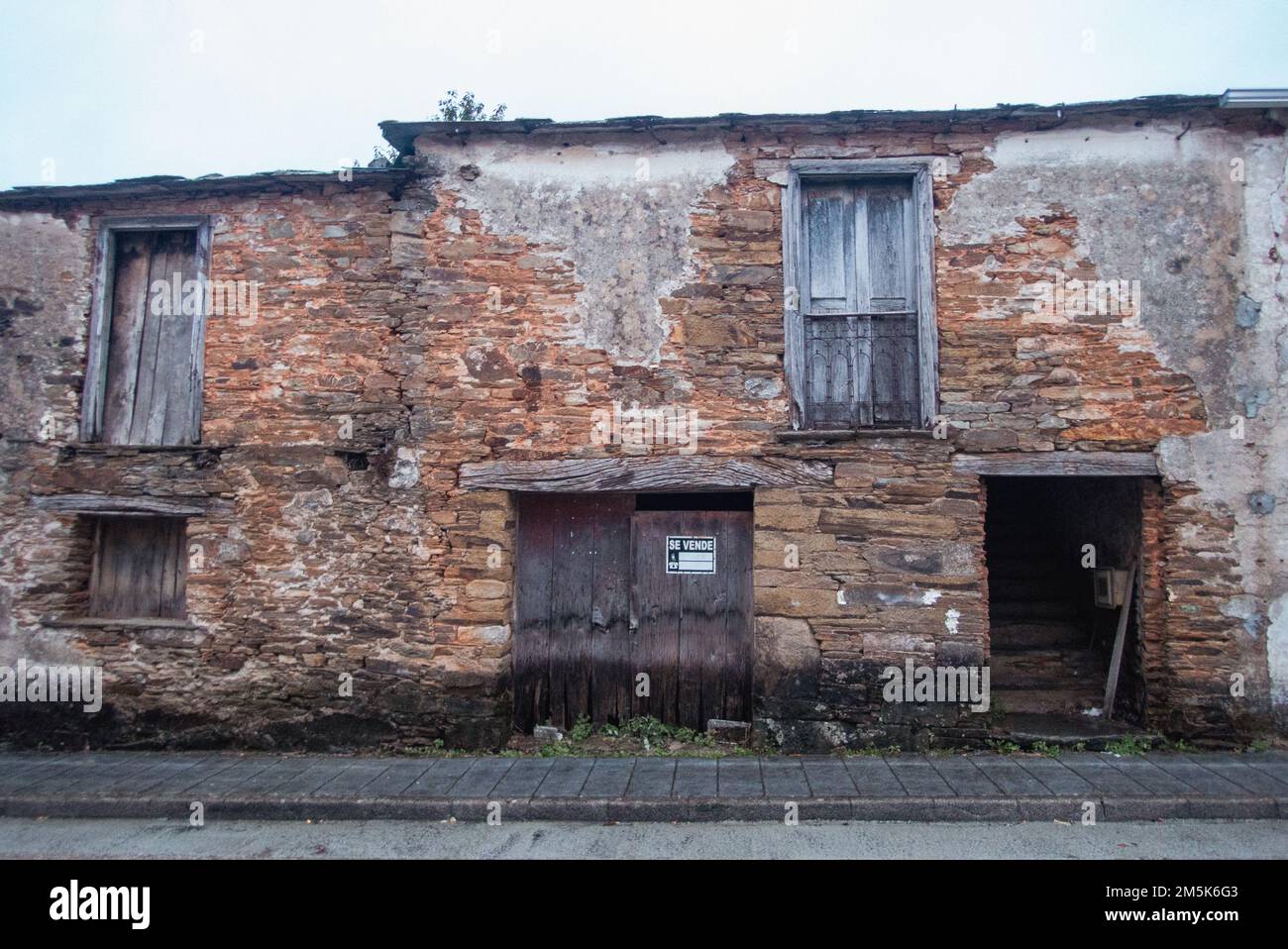 A ruin on sale. A derelict old farmhouse in the village Tricastela on the Saint James Way to Santiago de Compostela with a real estate agent's sign. Stock Photo