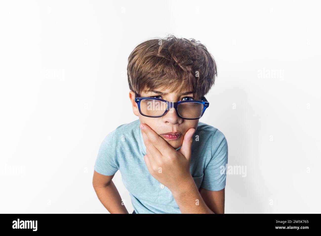 An exaggerated close up portrait of a funny little boy with glasses making a thinking face Stock Photo
