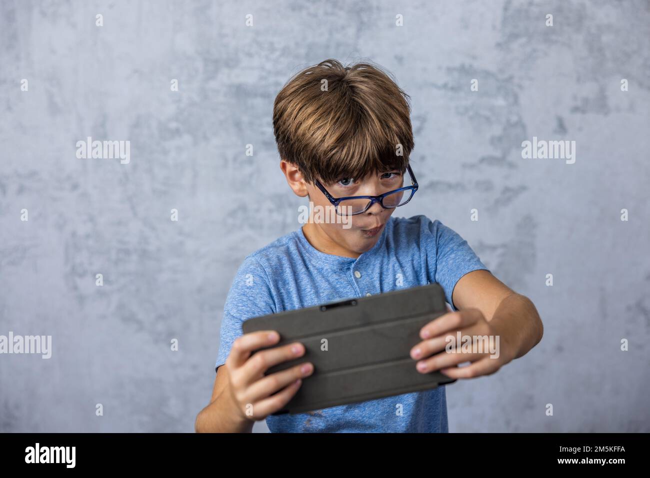 A little caucadian boy with glasses playing with his electronics tablet for screen time with copy space Stock Photo