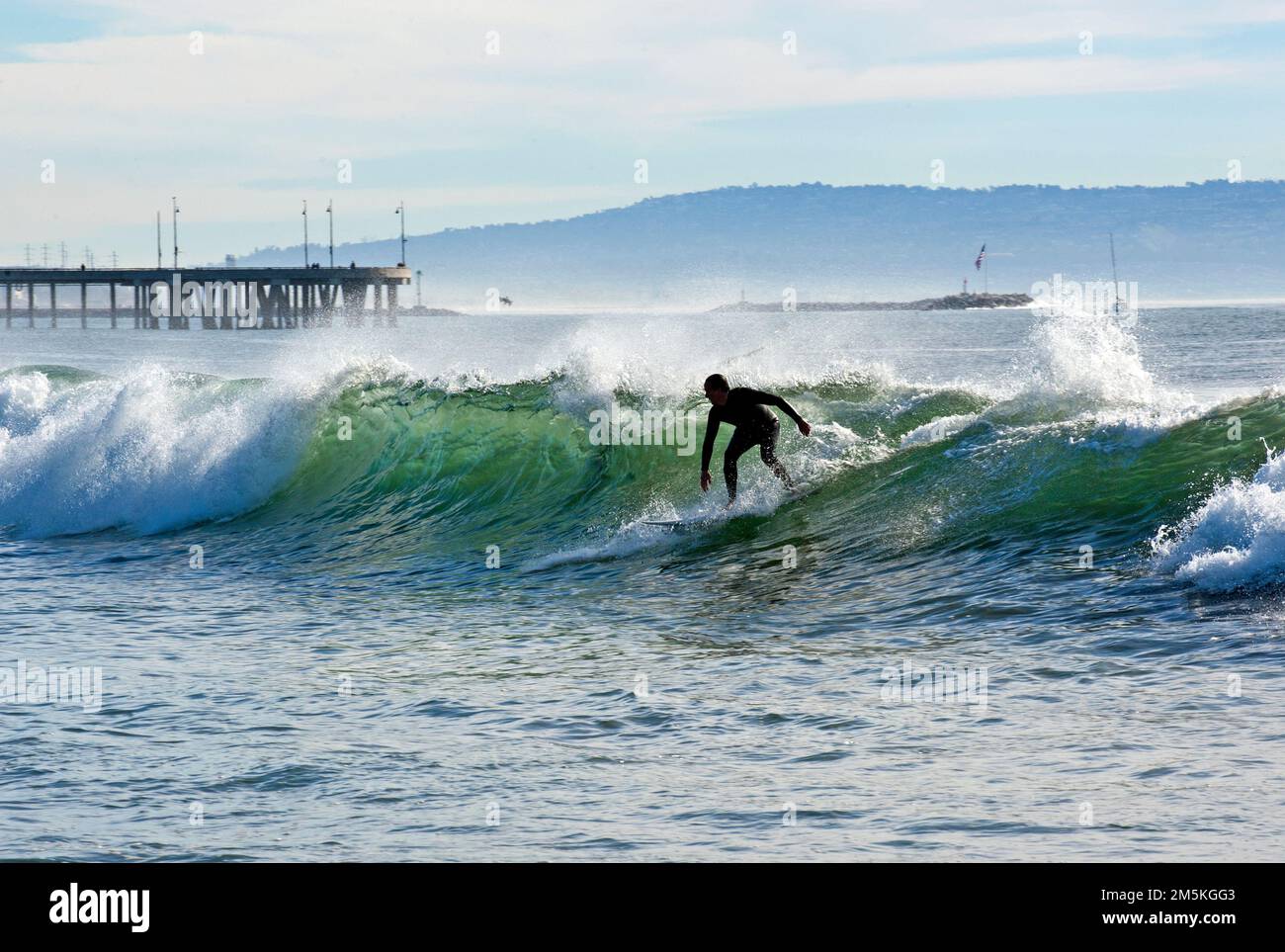 Surfer riding a wave near the Venice Pier with the Palos Verdes peninsula in the background in Southern California. Stock Photo