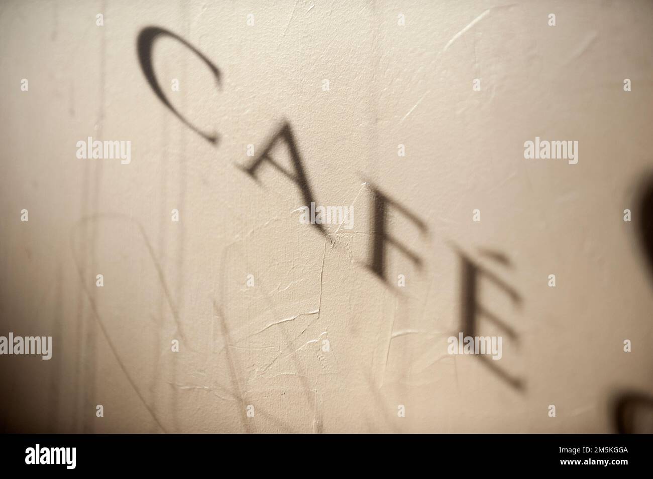 The shadow of the word Cafe from a window is projected across a wall inside a small restaurant. Stock Photo