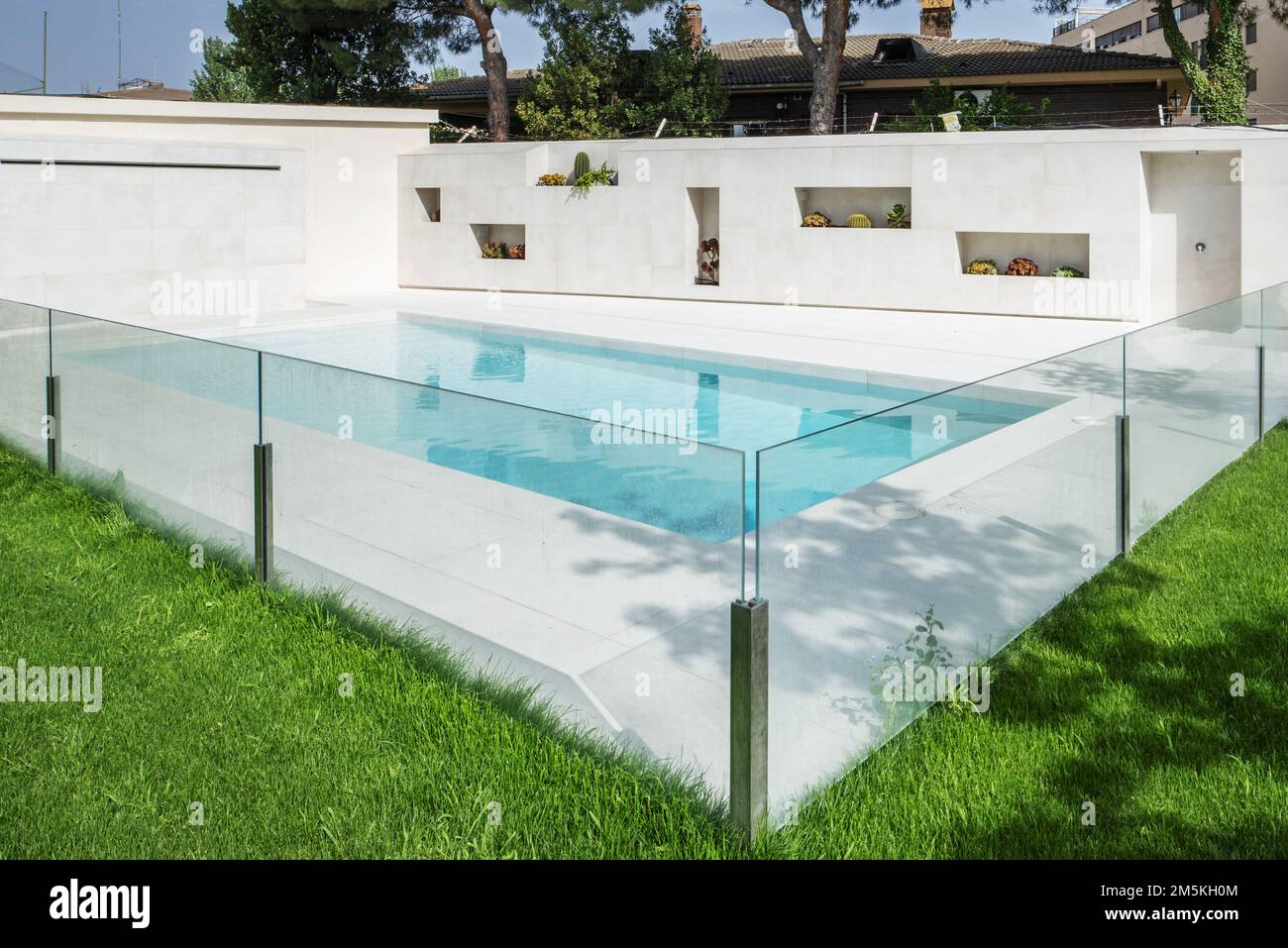 A white marble swimming pool with a glass railing, a lawned garden and flower pot niches in one