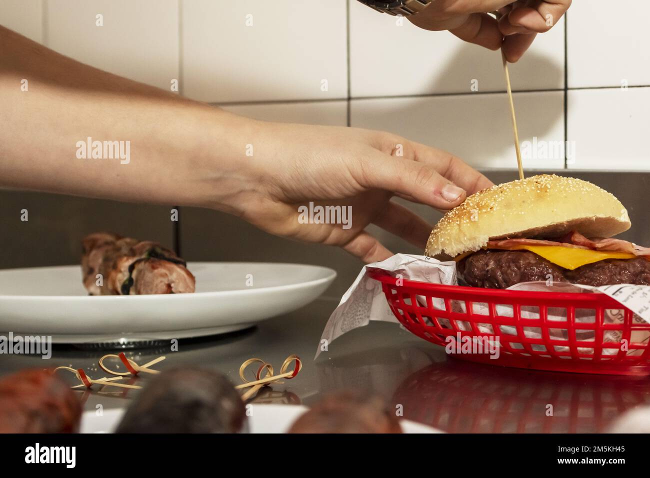 The hands of a chef assembling a beef burger cooking on charcoal grill