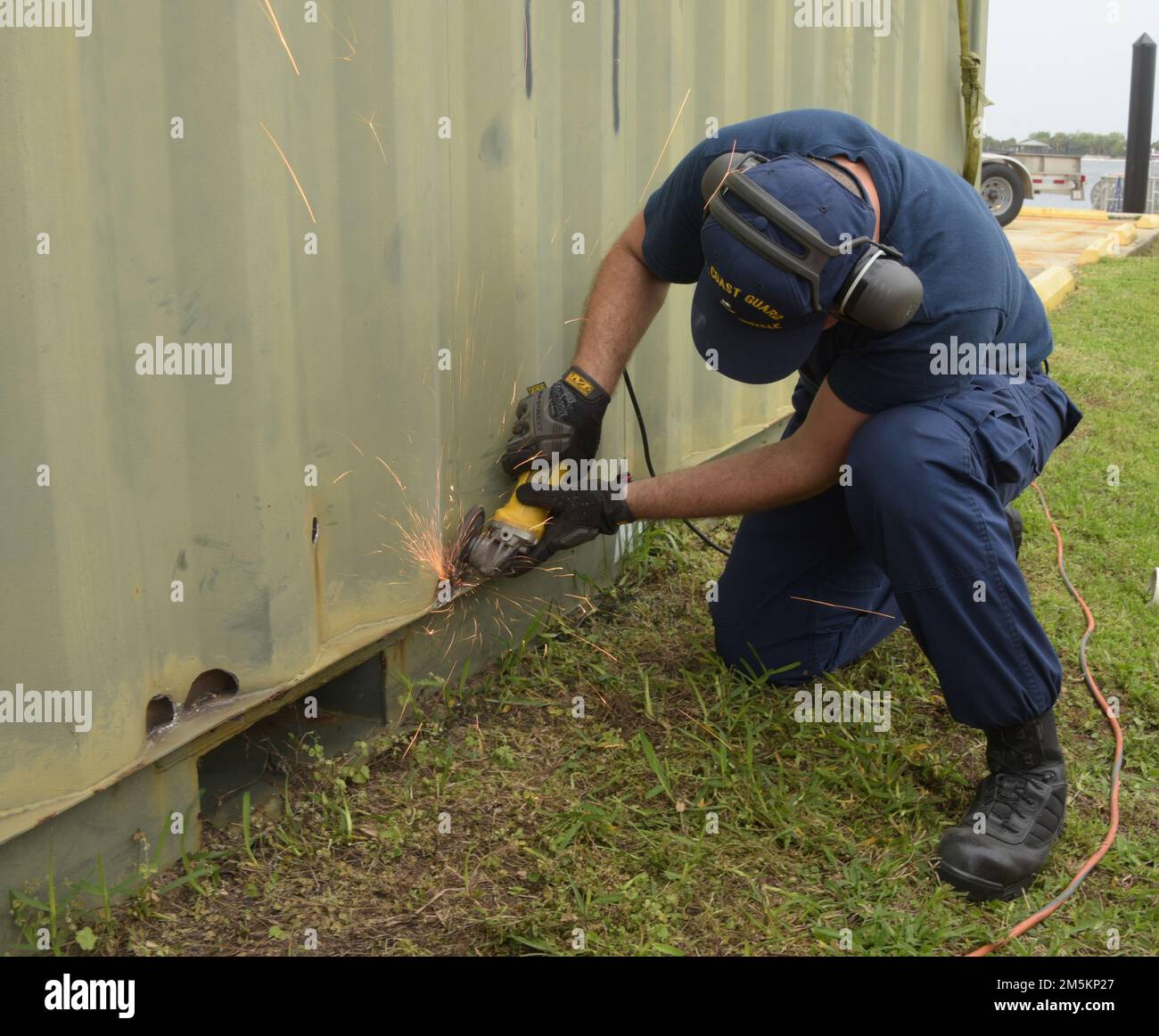 U.S. Coast Guard Petty Officer 3rd Class Hunter Parker, a damage controlman assigned to Sector Jacksonville, Florida, removes any rust from the outside of portable restroom facility being built at Sector Jacksonville, March 23, 2022. The portable restroom can be shipped to a location within the Sector Jacksonville area of responsibility where permanent restrooms are unavailable. Stock Photo