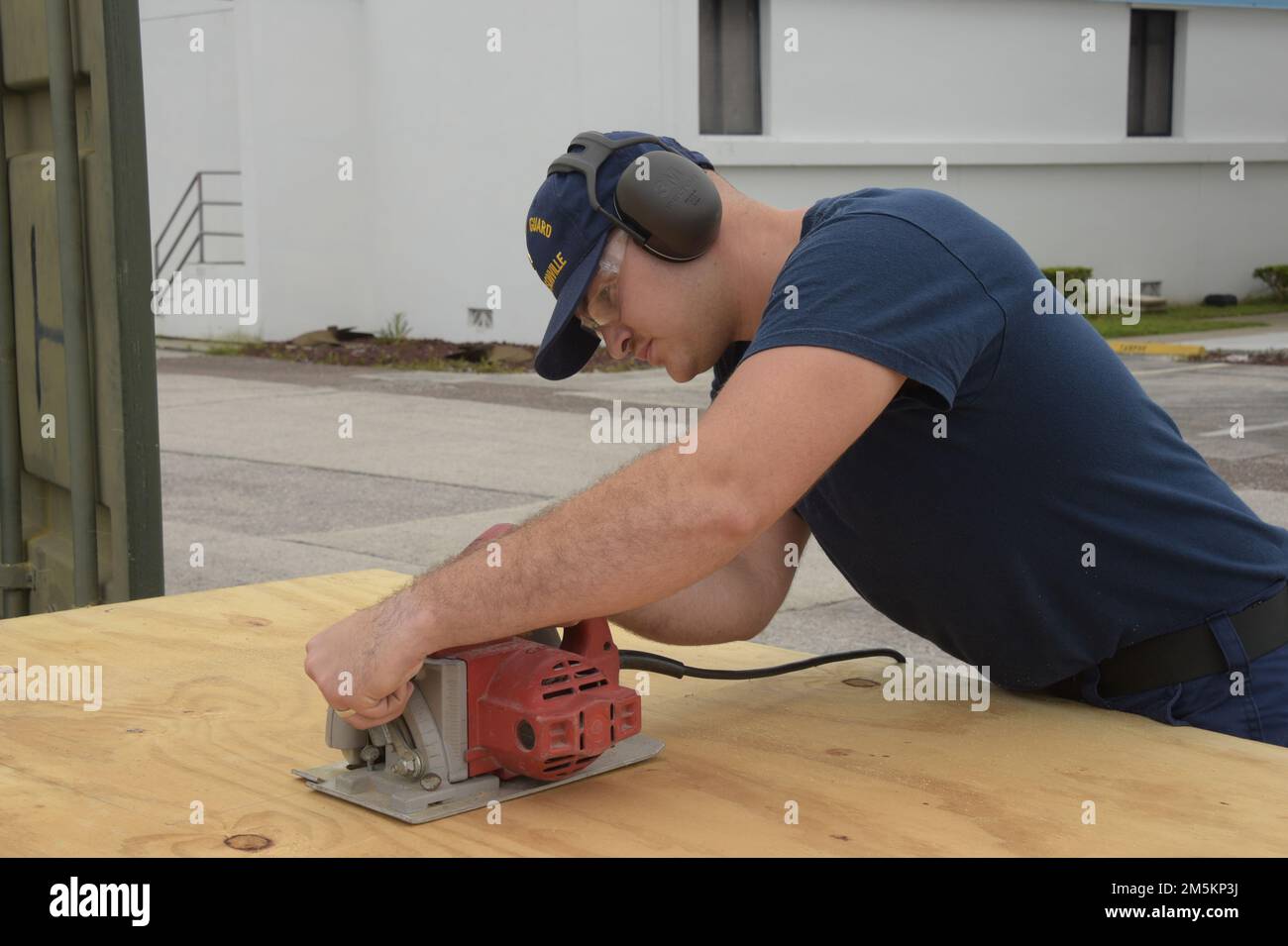U.S. Coast Guard Petty Officer 3rd Class Hunter Parker, a damage controlman assigned to Sector Jacksonville, Florida, cuts a piece of plywood to use in the construction of a portable restroom facility being built at Sector Jacksonville, March 23, 2022. The portable restroom can be shipped to a location within the Sector Jacksonville area of responsibility where permanent restrooms are unavailable. Stock Photo