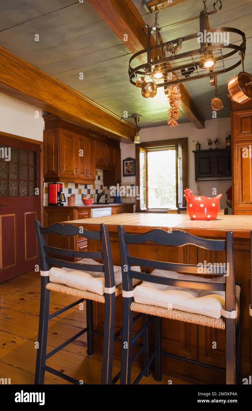 Tan ceramic top island with two old wooden bistro style weaved seat with cushions chairs in kitchen inside reconstructed 1840s log home. Stock Photo