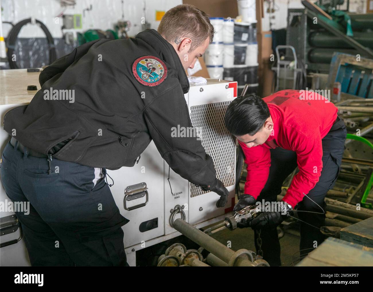 Aviation Ordnanceman Airman Robert Parsons, left, from Aurora, Colorado, and Aviation Ordnanceman Airman Andres Perez, from Fontana, California, both assigned to the 'Black Lions' of Strike Fighter Squadron (VFA) 213, secure a hydraulic servicing unit in USS Gerald R. Ford’s (CVN 78) hangar bay, March 23, 2022. Ford is underway in the Atlantic Ocean conducting flight deck certification and air wing carrier qualifications as part of the ship's tailored basic phase prior to operational deployment. Stock Photo