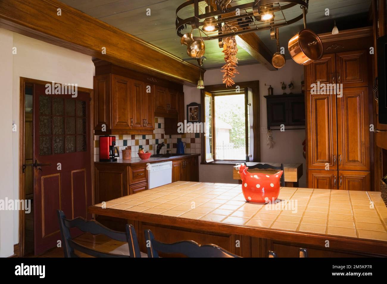 Tan ceramic top island with two old wooden bistro style weaved seat with cushions chairs in kitchen inside reconstructed 1840s log home. Stock Photo