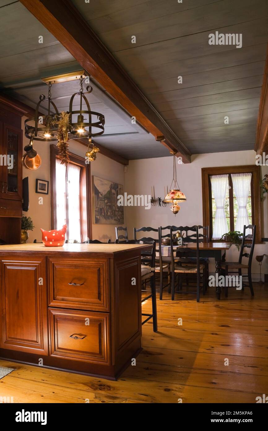 Tan ceramic top island and antique wooden dining table with high back weaved seat chairs in dining room inside reconstructed 1840s log home. Stock Photo