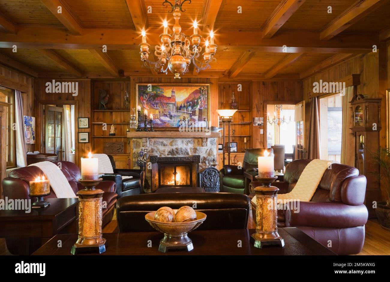 Lit stone fireplace and brown leather armchairs and sofas in living room inside old 1920s cottage style home. Stock Photo