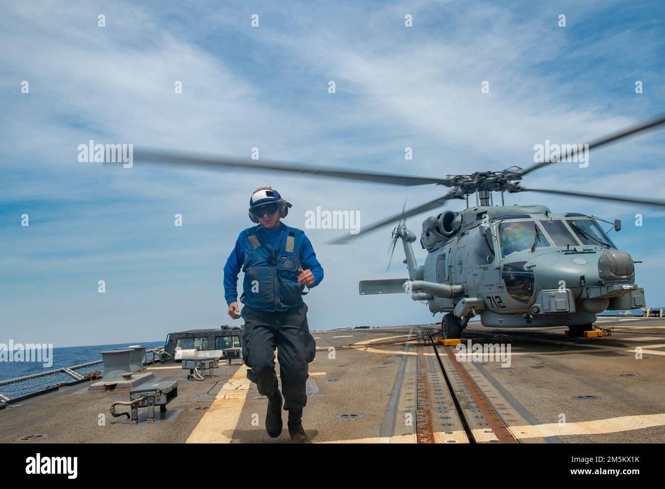 SOUTH CHINA SEA (March 23, 2022) Seaman Michael Blanchard, from Panama City Beach, Fla., returns to a safe distance after placing chocks and chains on a landing MH-60R Sea Hawk helicopter, assigned to the “Raptors” of Helicopter Maritime Strike Squadron (HSM) 71, on the flight deck of Arleigh Burke-class guided-missile destroyer USS Spruance (DDG 111). Abraham Lincoln Strike Group is on a scheduled deployment in the U.S. 7th Fleet area of operations to enhance interoperability through alliances and partnerships while serving as a ready-response force in support of a free and open Indo-Pacific Stock Photo