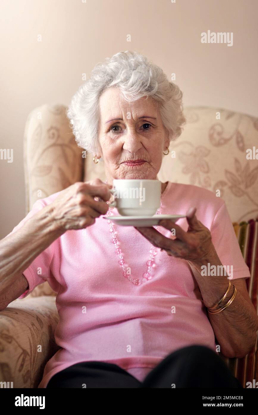 I still make a good cup of tea. Portrait of a senior woman having a warm beverage on a chair at home. Stock Photo