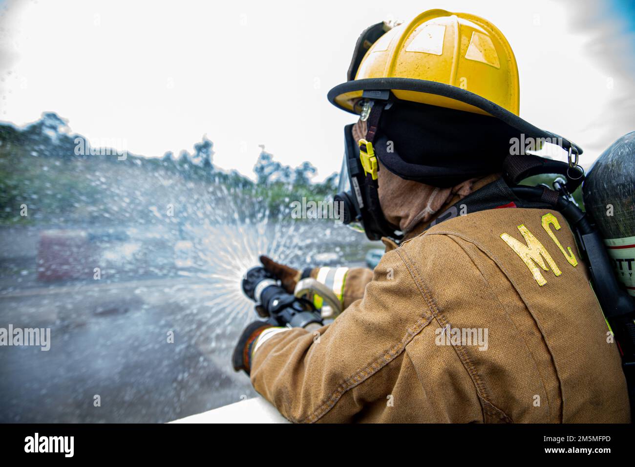 A firefighter with Marine Corps Installations Pacific Fire and Emergency Services expels excess water from a hose after bilateral live-fire training on Camp Hansen, Okinawa, Japan, March 25, 2022. MCIPAC F&ES and the Naha City Fire Department assembled and conducted live-fire training to compare the different firefighting techniques and methods each department uses to accomplish the same mission. Stock Photo