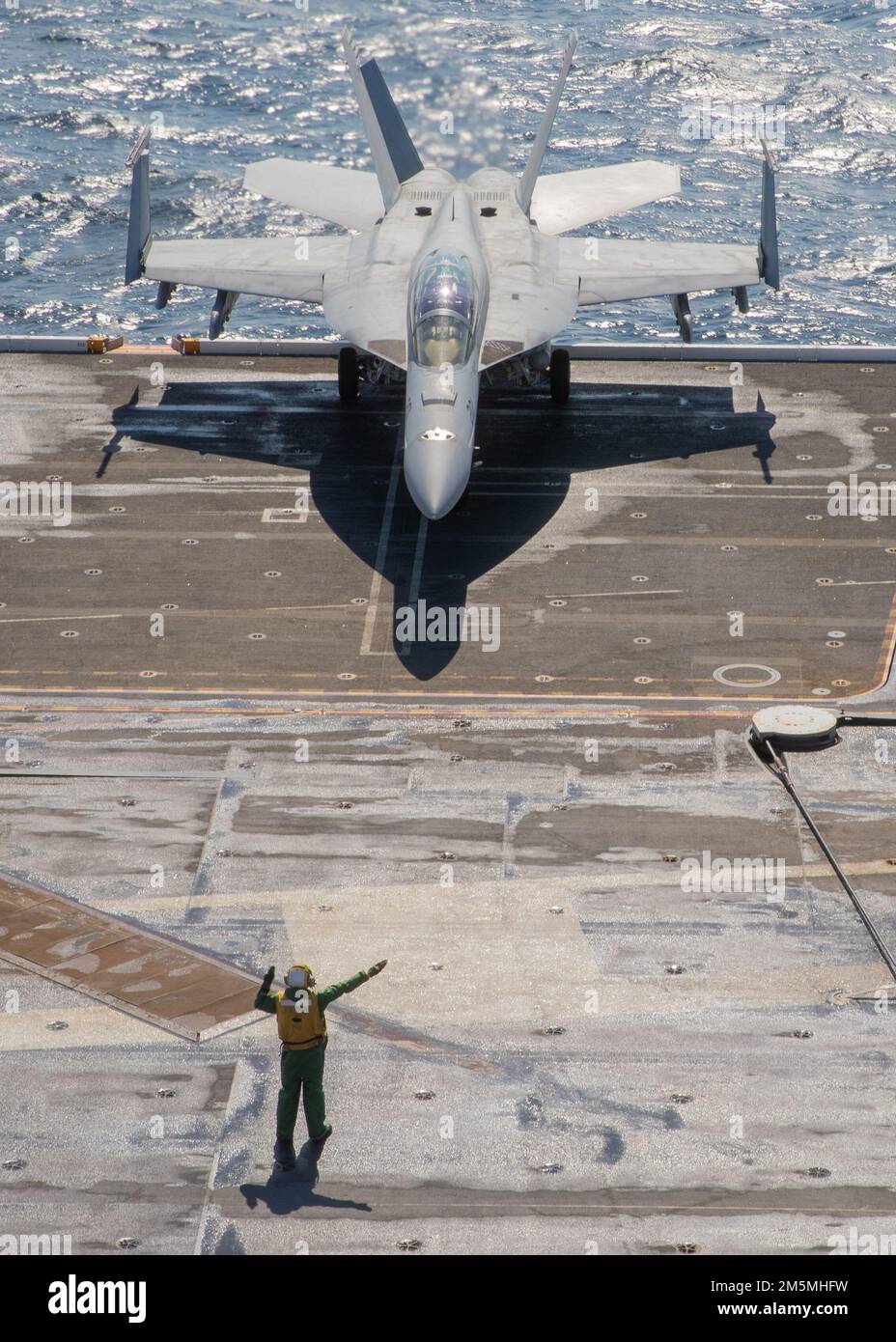 A Sailor assigned to USS Gerald R. Ford's (CVN 78) air department, directs an F/A-18F Super Hornet, attached to the 'Blacklions' of Strike Fighter Squadron (VFA) 213, during flight operations on Ford’s flight deck, March 25, 2022.  Ford is underway in the Atlantic Ocean conducting flight deck certification and air wing carrier qualification as part of the ships tailored basic phase prior to operational deployment. Stock Photo
