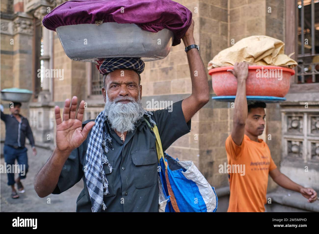 A porter with a tray of fish on his head, at Chhatrapati Shivaji Maharaj Terminus (CMST), in Mumbai, India, stopping to greet the photographer Stock Photo