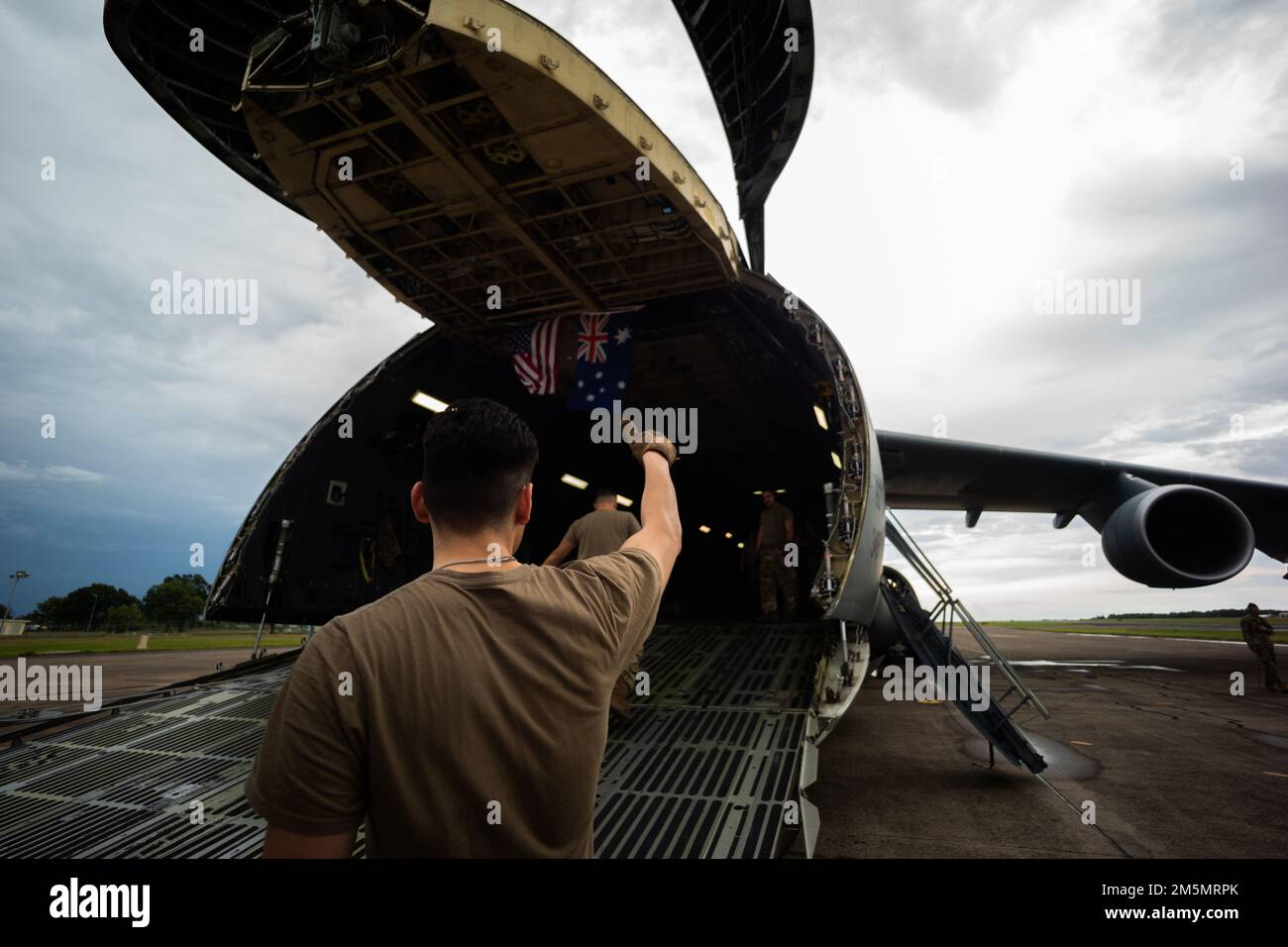 A U.S. Airman with 22nd Airlift Squadron, Air Mobility Command, gives the thumbs up signal to the loadmaster of a Lockheed C-5M Super Galaxy during a movement of equipment at Royal Australian Air Force Base Darwin, NT, Australia, March 27, 2022. The C-5M will be moving U.S. Marine Corps equipment from Darwin to Okinawa, Japan, an initiative by Marine Rotational Force-Darwin 22, ensuring the equipment is operational to maintain a credible crisis and contingency-ready force that can contribute to a free and open Indo-Pacific region. Stock Photo