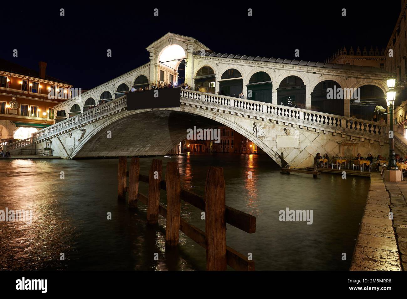 Night view of the Venetian Grand Canal with the Rialto Bridge in the background with people having dinner under the bridge in the moonlight, Venice, I Stock Photo