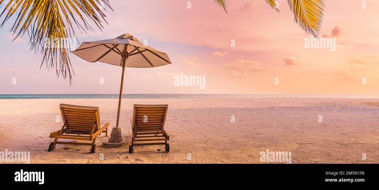 Beautiful panoramic nature. Tropical beach sunset as summer island landscape chairs umbrella palm leaves calm sea shore, coast. Luxury travel panorama Stock Photo